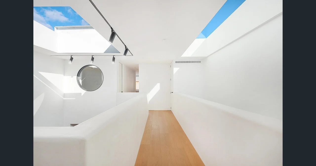 Two rectangular skylights revealing blue sky above a white hallway and stairwell with a timber floor